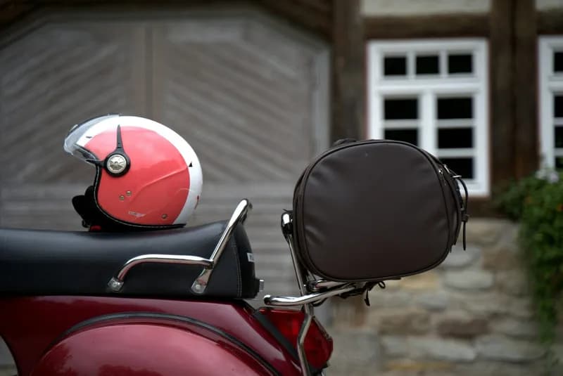Casque jet posé sur la selle d'un scooter rouge de style Vespa